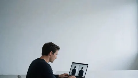 Professional photographer reviewing images on a laptop in a minimalist studio with white walls and cool tones, with ample copy space at the top for website text.