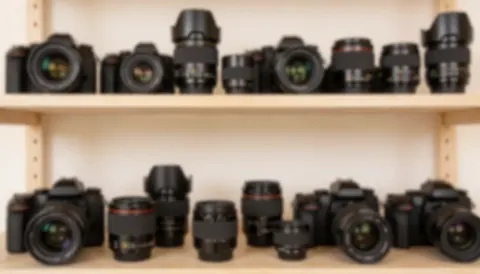 Soft focus background of a photography studio shelf filled with multiple cameras and lenses, featuring warm tones suitable for text and graphic design.