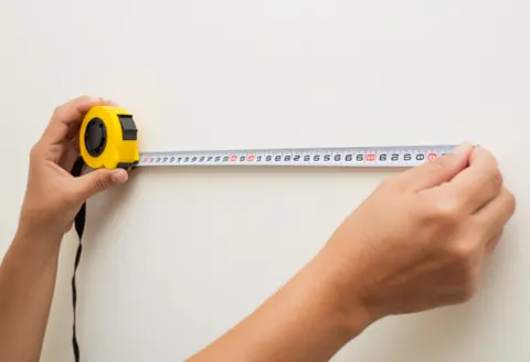 Close-up of hands using a tape measure to check wall dimensions for property assessment