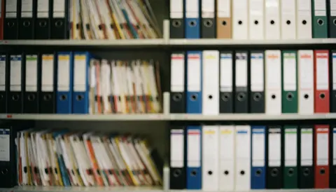 Shelves filled with colorful file folders in an accounting office, providing a soft, professional, and organized background suitable for text overlays.