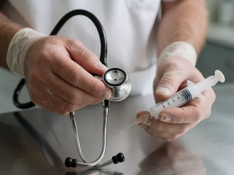 Gloved hands holding a stethoscope and syringe on a metal exam table in a veterinary clinic setting