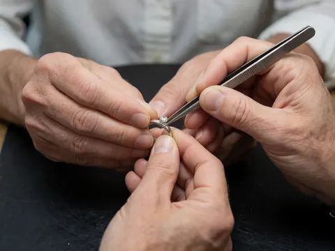 Close-up view of a diamond being set in silver using tweezers, highlighting precision jewelry craftsmanship against a dark background