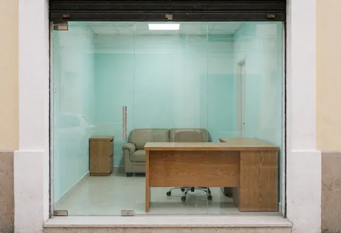 View of a security office interior featuring an oak desk, sofa, and turquoise walls, seen through the storefront window from the street.