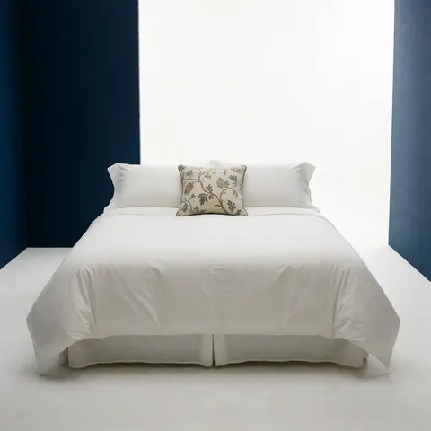 A neatly made bed featuring crisp white linens and a decorative pillow against a blue wall in a luxury hotel room
