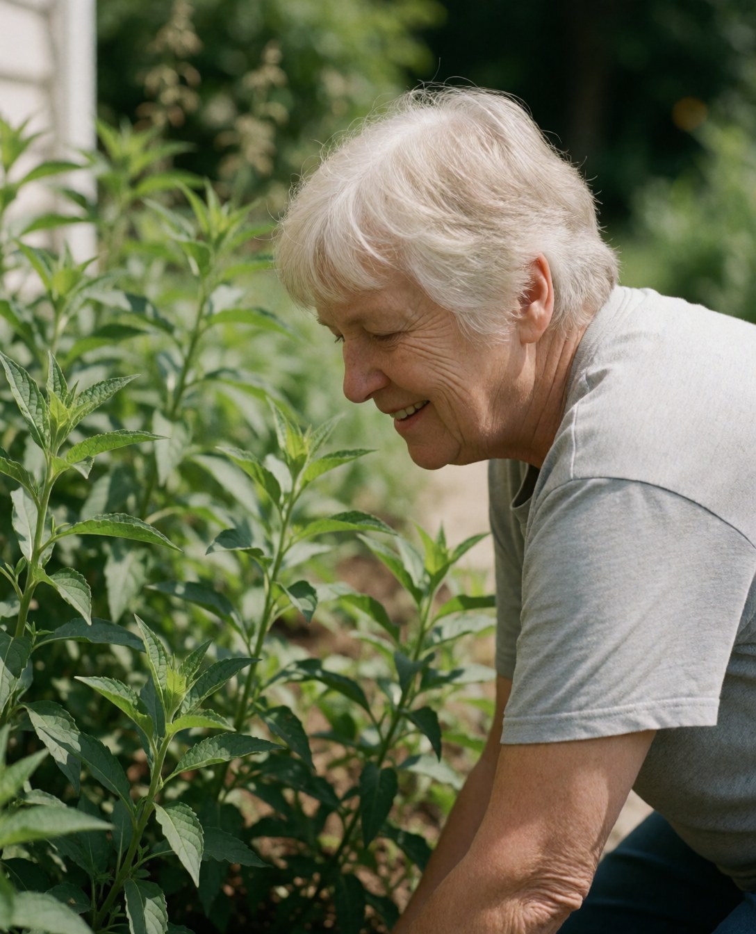 A smiling woman stands in a sunny garden surrounded by green plants and flowers, looking satisfied with the landscaping work.