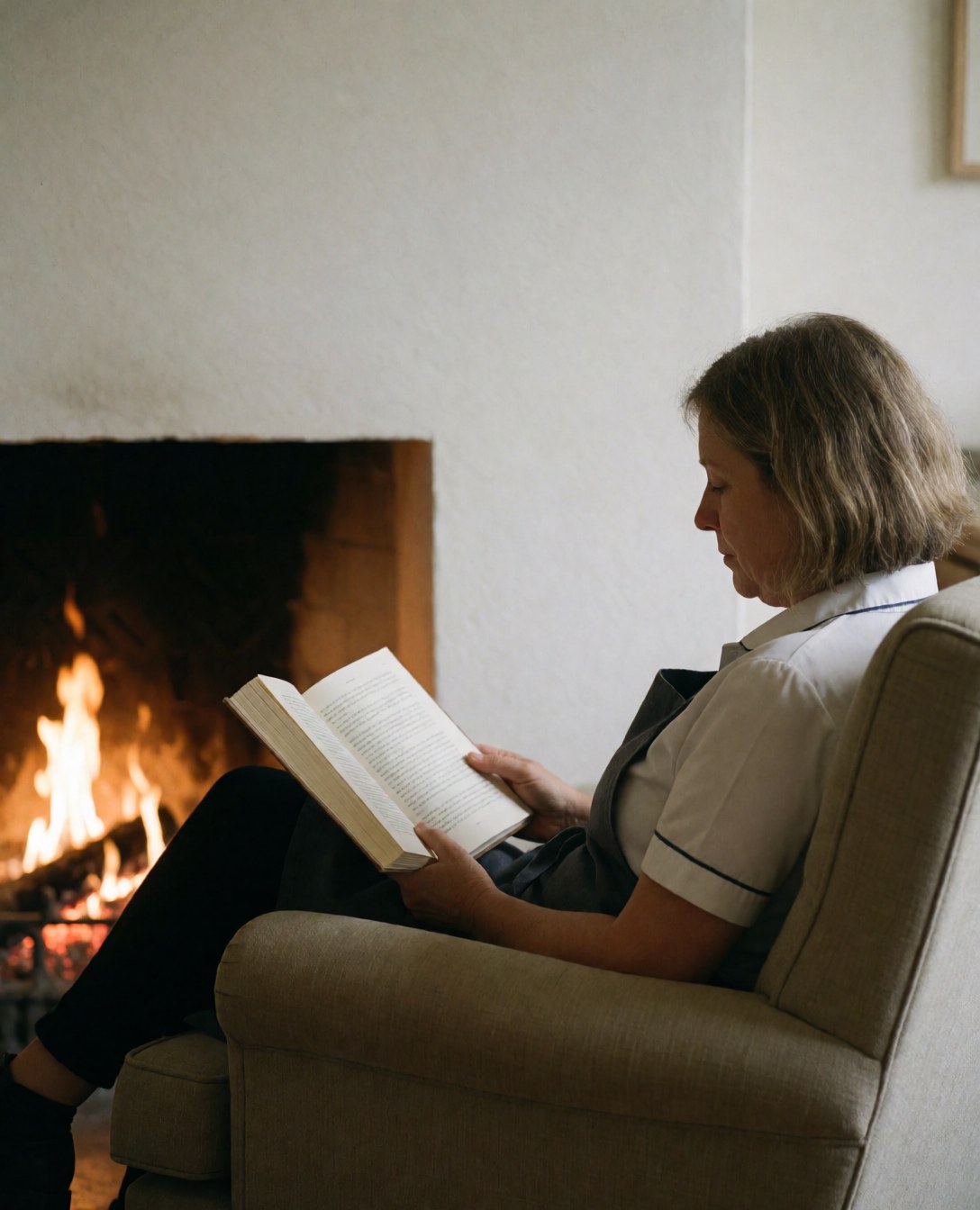 A relaxed female guest enjoying quiet time by a fireplace in a comfortable boutique hotel setting