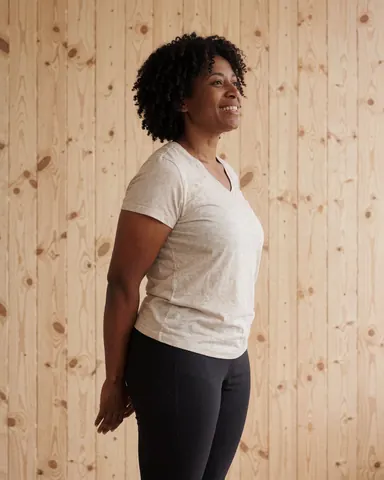 A smiling woman in athletic wear stretching her arms and legs after a yoga or pilates session in a bright, calm studio with a wooden wall background.