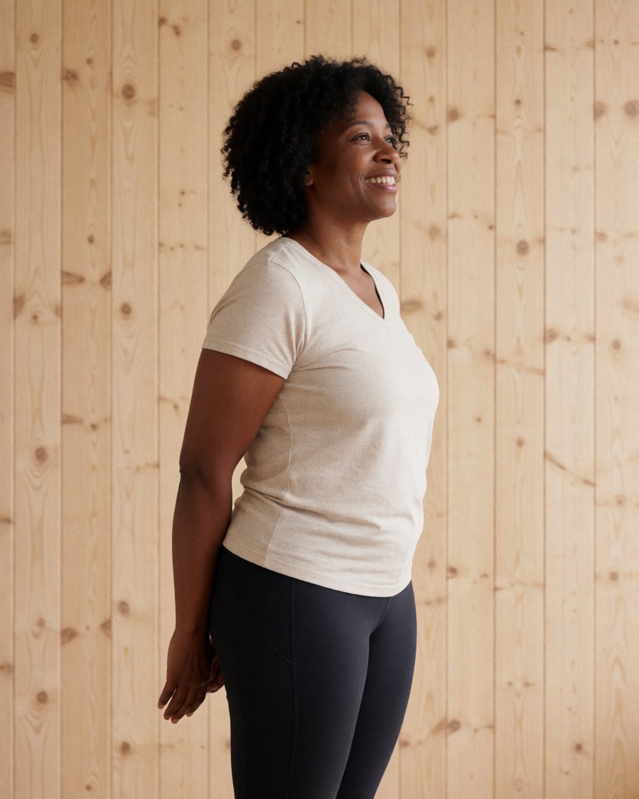 A smiling woman in athletic wear stretching her arms and legs after a yoga or pilates session in a bright, calm studio with a wooden wall background.
