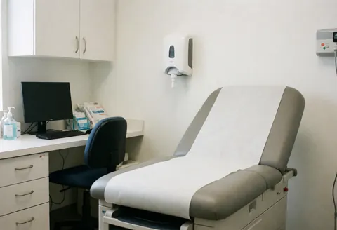 A clean and professional medical examination room featuring a white exam table, computer, and medical supplies ready for patient care