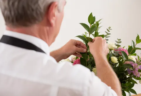A florist arranging a bouquet of roses and green leaves in a softly lit studio, showcasing the professional service process.