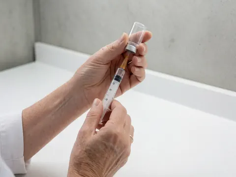 Close-up of adult hands carefully filling a medical syringe from a glass vial against a clean clinical background for a medical clinic