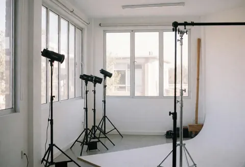 Bright photo studio featuring white walls, large windows, professional lighting, and a white background for showcasing photography services.