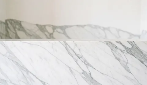 Close-up view of a white and gray marble surface with natural veining patterns, serving as an elegant background for real estate marketing materials.