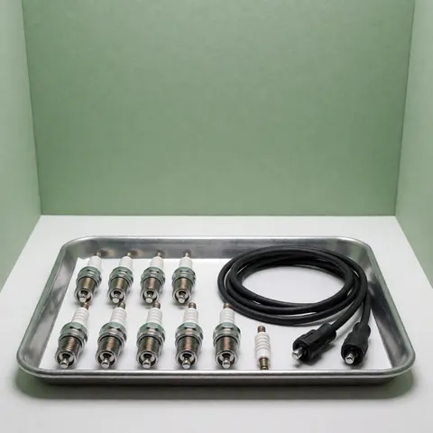 A set of clean spark plugs and ignition cables arranged neatly on a metal tray against a green background for automotive repair product display