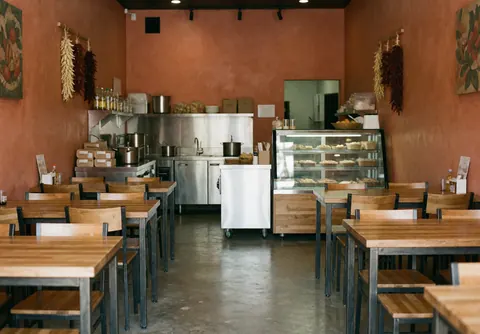 Empty restaurant dining area featuring wooden tables, metal chairs, terracotta walls, and a display case, ready for customers.