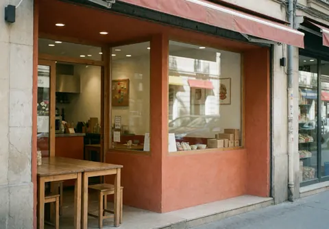 Restaurant exterior featuring terracotta walls, large windows, and wooden tables. The inviting interior is visible through the glass.