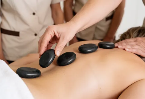 A therapist uses smooth hot basalt stones to perform a relaxing massage on a client's back during a spa treatment session