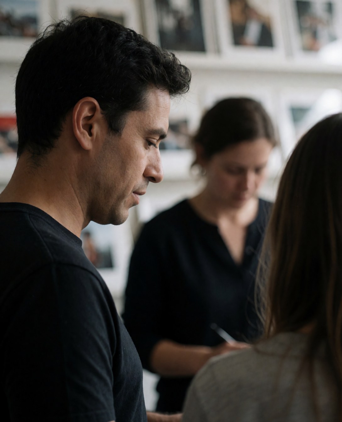A professional photographer reviews photographs in a studio with prints on the walls and another person working in the background.