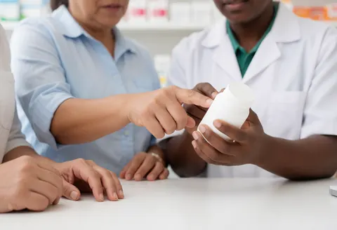 A pharmacy professional holding a medicine bottle and explaining its use to a client in a retail setting