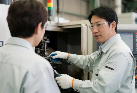 A technician in safety gear explains industrial machinery to a client in a realistic factory setting