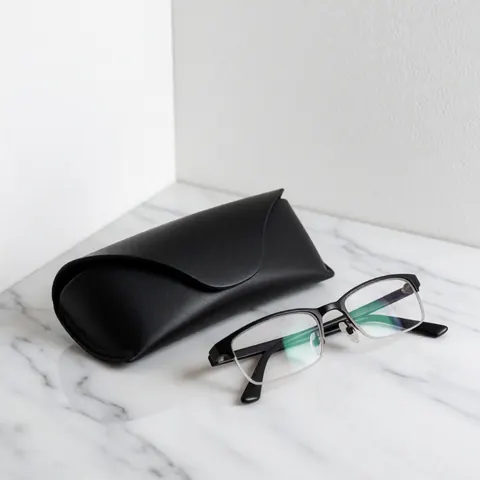 Black framed reading glasses and a black case resting on a white marble surface with soft minimalist lighting for optical store product display