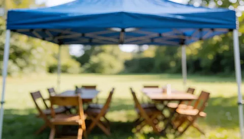 Blue sky above wooden tables and chairs on a green field with natural light and blurred background for text overlays