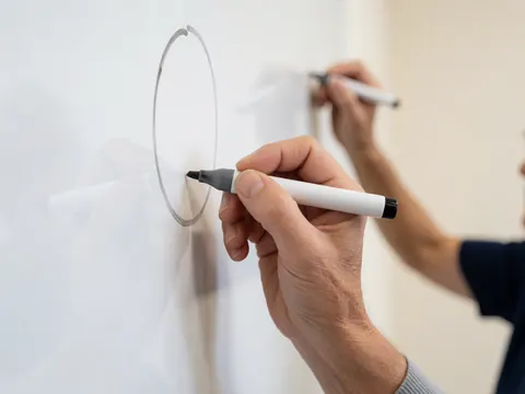 Adult hand drawing a circle with a marker on a whiteboard in a clean modern setting ideal for nutrition and planning