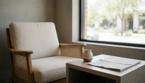 A spacious hotel lobby featuring a comfortable armchair, a table with a map and ceramic decor, and natural light creating a welcoming atmosphere.