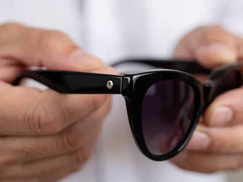 Detailed view of the metal hinge on black acrylic cat eye sunglasses held in hands with a blurred background