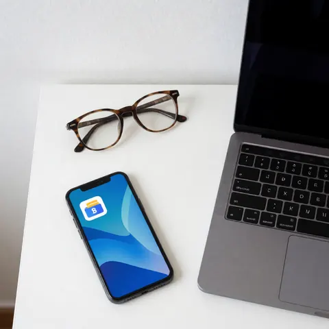 Smartphone displaying banking app, laptop and eyeglasses on a clean white desk for finance and banking