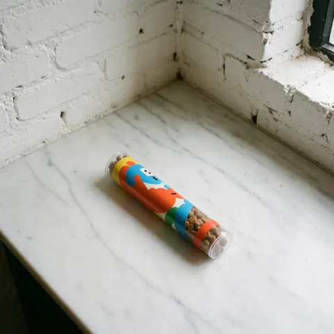 Colorful dog treat tube placed on a white marble countertop with a white brick wall background and natural lighting
