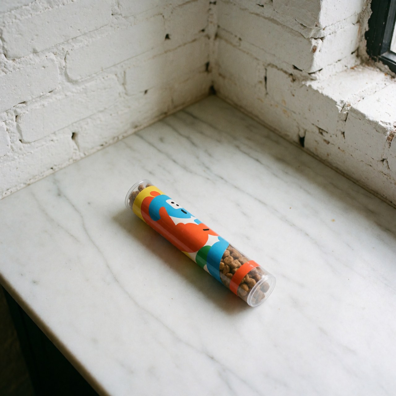 Colorful dog treat tube placed on a white marble countertop with a white brick wall background and natural lighting