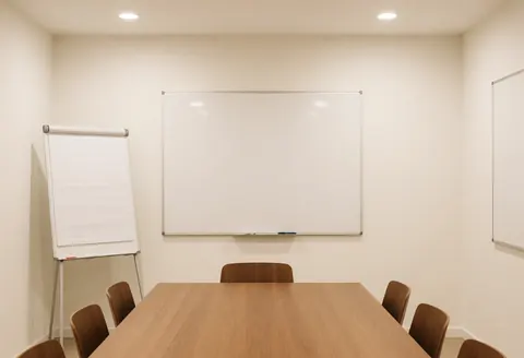 Modern minimalist meeting room featuring a wooden table, chairs, and whiteboards, ideal for business planning and strategic discussions in a professional environment.