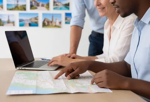 A travel agent and a happy client review a map and computer in a bright office while planning a trip.