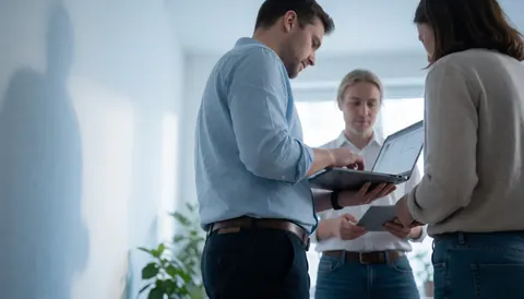 Three developers working together on a laptop in a bright modern office, highlighting teamwork and technical collaboration for software startups.