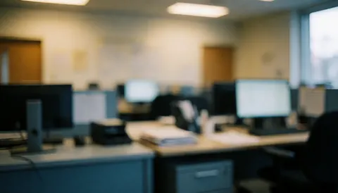 A soft focus background of an empty office workspace featuring a desk, computer monitor, and chair in neutral tones suitable for professional presentations