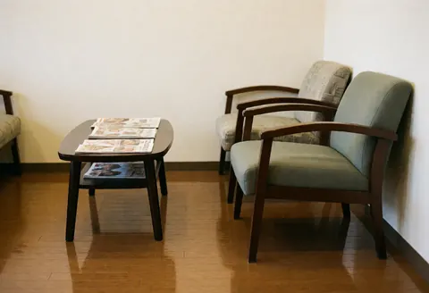 Side view of a clean and comfortable barbershop waiting area featuring polished wood floors, white walls, and seating for clients
