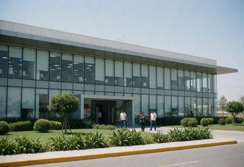 Modern industrial factory with glass facade, green garden, people walking outside, blue sky, main entrance, clean professional architecture