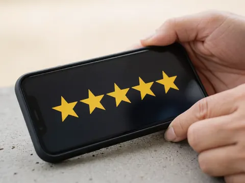 A hand holds a smartphone displaying five yellow stars on the screen, resting on a concrete surface, symbolizing customer satisfaction and digital marketing.