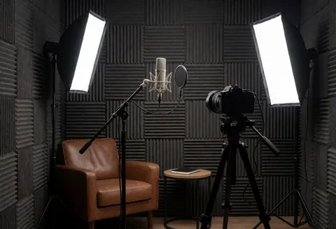 Professional recording studio featuring a microphone, camera on a tripod, leather chair, and lighting equipment.