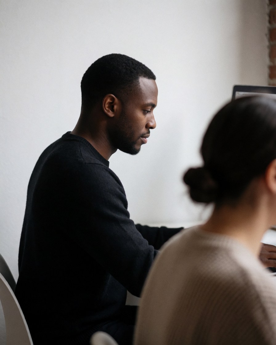 A focused professional man working on a laptop computer at a modern office desk with soft lighting and a white wall background