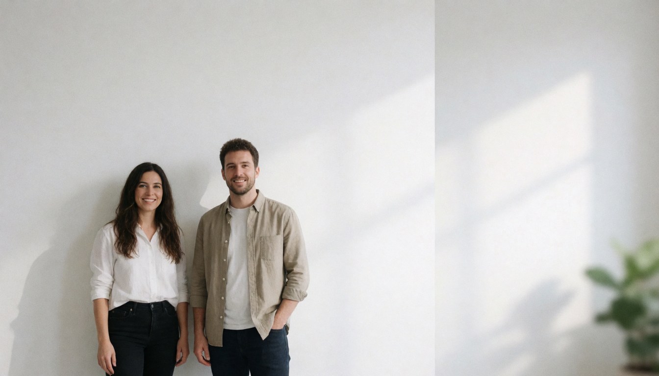 A smiling couple poses against a white wall with natural light and soft shadows, ideal for corporate backgrounds or service presentations.