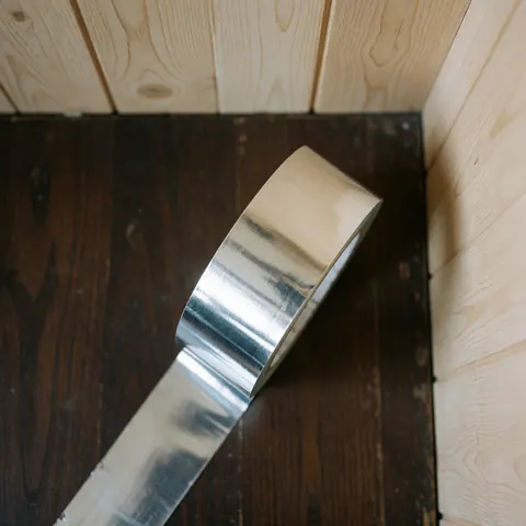 A roll of silver aluminum tape resting on a wooden surface, commonly used for HVAC duct sealing and air conditioning installation.