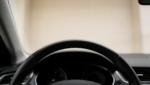 Blurred black steering wheel and dashboard inside a car, providing copy space at the top for driving school text backgrounds