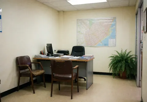 Empty driving school office featuring a desk, computer, chairs, and various city and route maps on the wall and floor