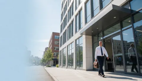 A male accountant carrying a briefcase walks toward the entrance of a modern corporate building under a clear blue sky.