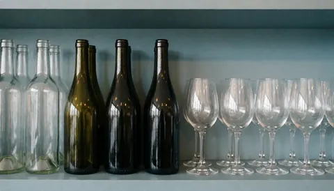 Wine bottles and glasses arranged on a shelf in a bar with blue and gray tones, creating a serene background suitable for advertising text.