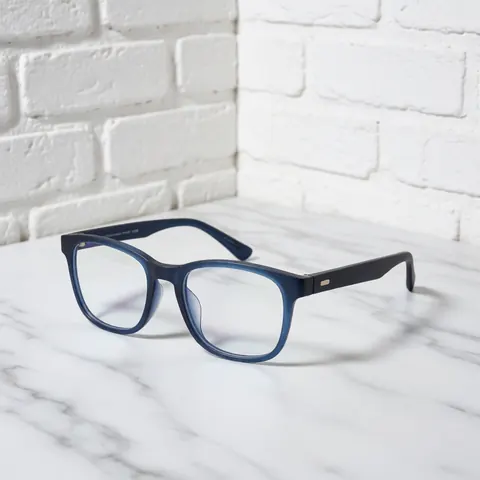 A pair of modern blue light blocking eyeglasses resting on a white marble surface with a brick wall background, ideal for optical store product displays.