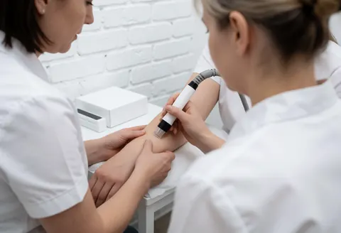 A professional esthetician performs laser therapy on a client's skin in a clinical setting, focusing on the treatment area with specialized equipment.