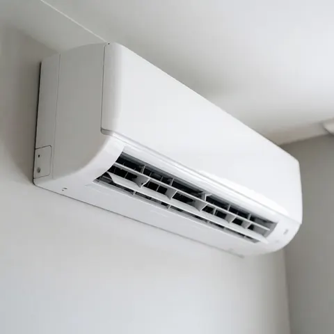 Close-up of a sleek white indoor air conditioning unit mounted on a light gray wall, featuring clean lines and minimalist design with natural lighting.